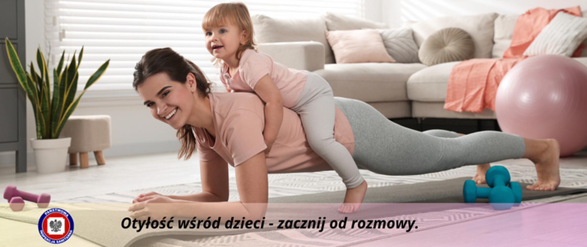 W salonie na macie ćwiczy "deskę" uśmiechnięta mama, na jej plecach leży dziewczynka. Obie są tak samo ubrane. Poniżej na przeźroczystym pasku czarny napis Otyłość wśród dzieci - zacznij od rozmowy, z jego lewej strony logo Państwowej Inspekcji Sanitarnej.