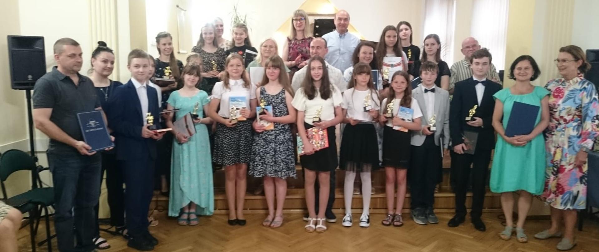 Grupa absolwentów wraz z rodzicami pozujących do zdjęcia grupowego podczas koncertu pożegnania absolwentów w PSM I st. w Kłodzku 21 czerwca 2023