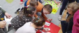 Dzieci siedzą na podłodze i układają obrazki z wizerunkiem różnych przekąsek na czerwonej oraz zielonej planszy.
