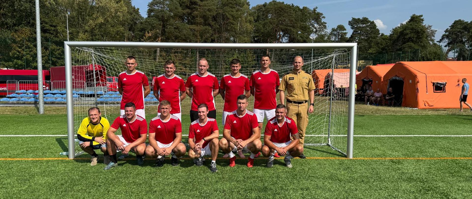 Wspólne zdjęcie zawodników z KP PSP w Makowie Mazowieckim wraz z Komendantem na boisku na tle bramki.