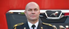 St. ogn. Bogusław Kwiecień na tle samochodu pożarniczego.
