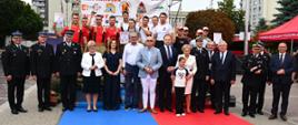 Grupa uczestników i organizatorów XXXV Memoriału im. płk. poż. Andrzeja Bazanowskiego pozuje do wspólnego zdjęcia. Na tle baneru zawodów stoją strażacy w sportowych strojach i mundurach, a przed nimi zaproszeni goście i przedstawiciele PSP oraz samorządu. W tle widoczny namiot z napisem „Komenda Wojewódzka Państwowej Straży Pożarnej”.