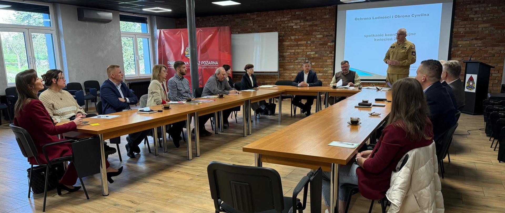 Uczestnicy spotkanie siedzą przy stołach na sali szkoleniowej.