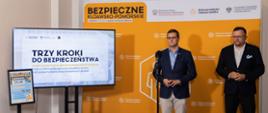 Wojewoda Michał Sztybel oraz zastępca dyrektora WBZK Ireneusz Nitkiewicz podczas konferencji, w tle ścianka OLiOC