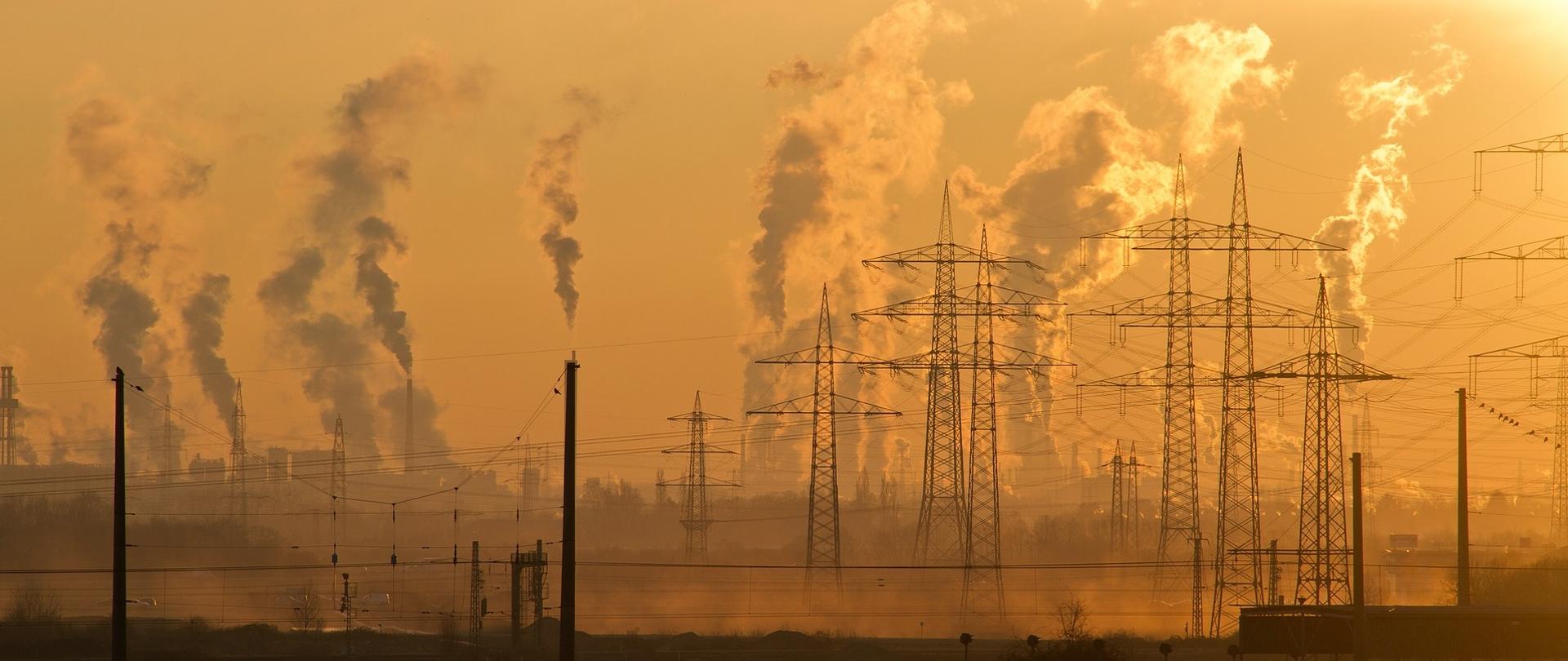 Zdjęcie przedstawia krajobraz przemysłowy z dymiącymi kominami w tle.