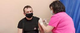 Zdjęcie przedstawia jednego z funkcjonariuszy KP PSP w Gołdapi podczas przyjmowania szczepionki przeciw COVID–19