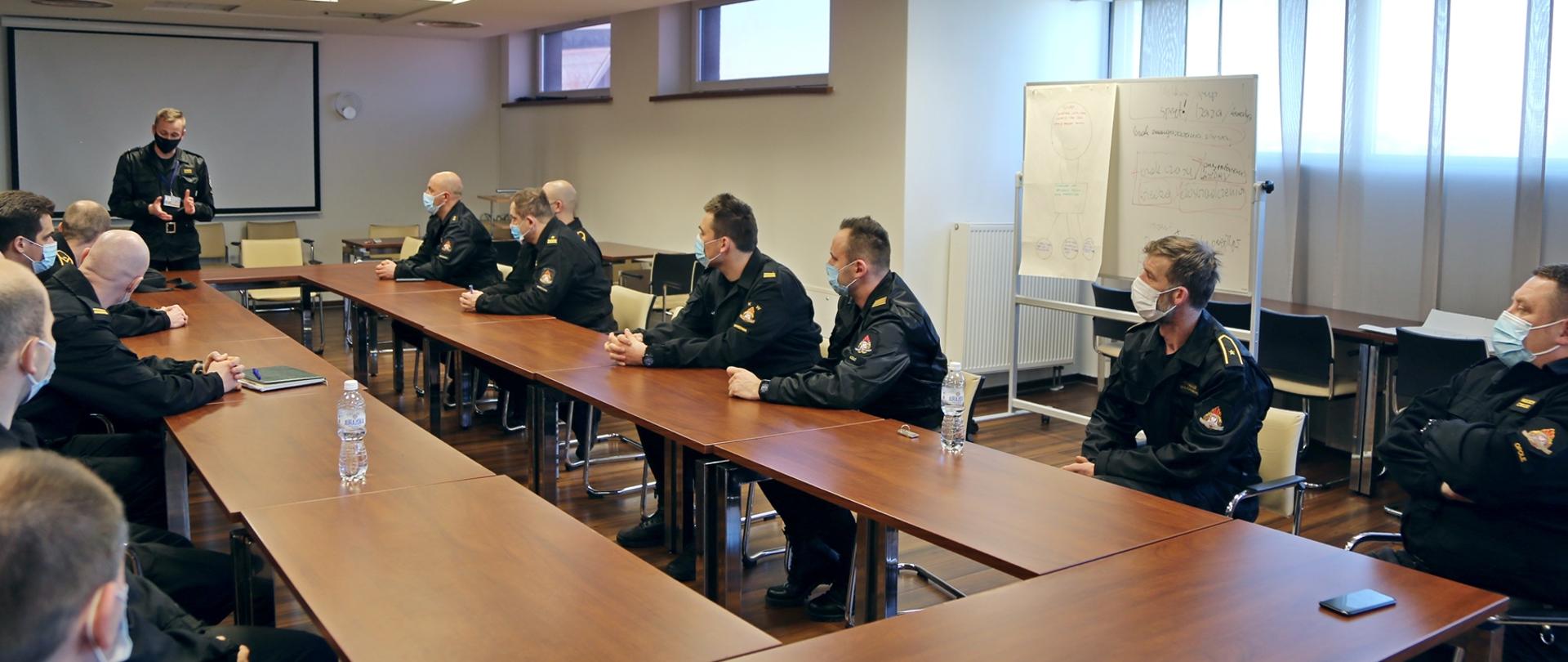 Uczestnicy warsztatów siedzą w dwóch rzędach ławek naprzeciwko siebie, w głębi Zastępca Komendanta Centralnej Szkoły PSP