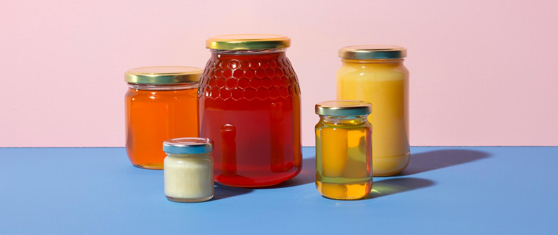 Kilka słoików różnych miodów na stole.