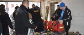 Sprzęt pożarniczy dla ukraińskich strażaków. Komenda Powiatowa PSP w Rawiczu. Strażacy przygotowują do transportu zebrany sprzęt. Na europalecie owijają folią poukładane obuwie strażackie i torbę medyczną.