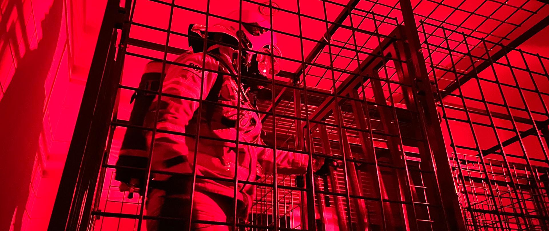 Na czwartym zdjęciu strażak w ubraniu specjalnym
z założoną na twarzy maską i aparatem powietrznym na plecach oraz w hełmie chroniącym jego głowę pokonuje przeszkody w komorze dymowej. Przeszkody wykonane są z metalowych elementów. Test odbywa się w całkowitym zaciemnieniu
i zadymieniu.