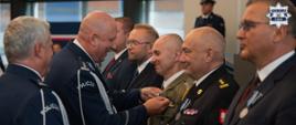 Inspektor Policji przypina medal do klapy munduru pułkownika Wojska Polskiego, stojącego w rzędzie wraz z innymi odznaczanymi osobami