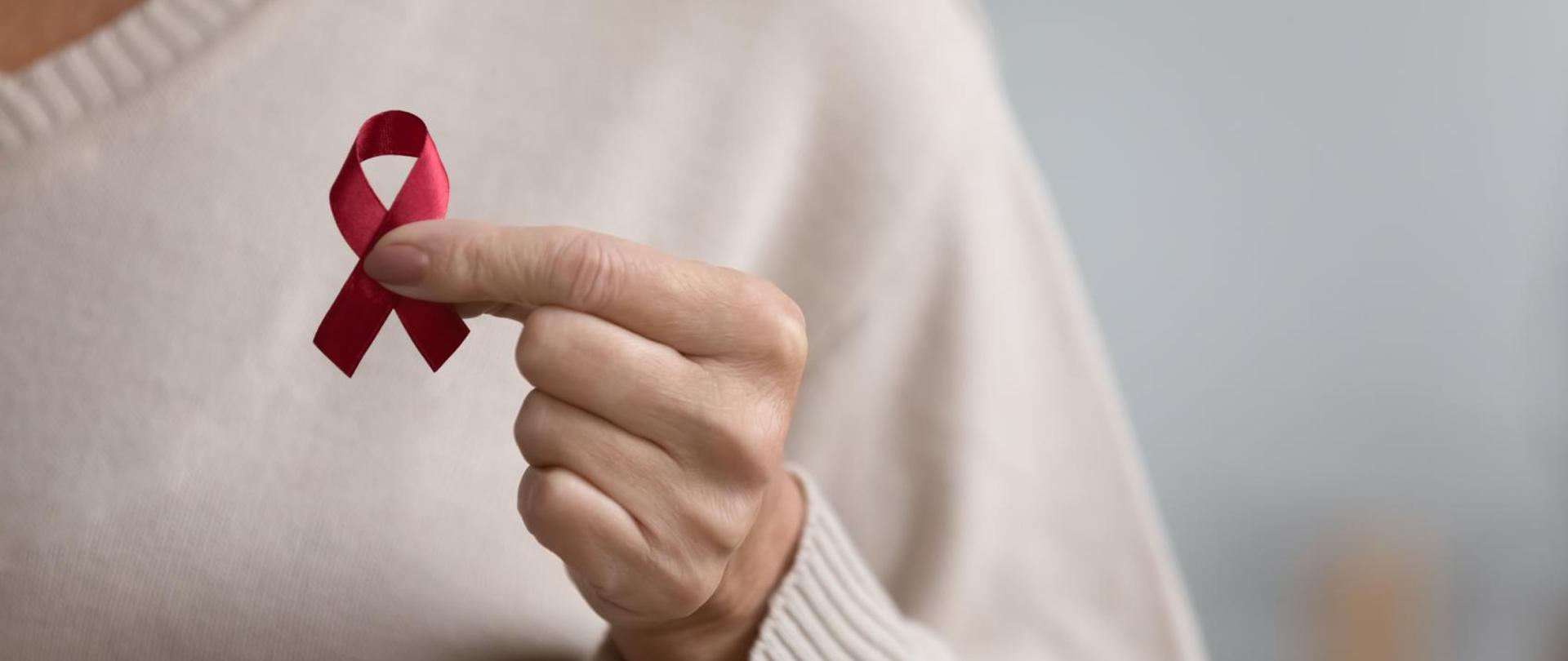 zdjęcie ręki trzymającej różową wstążkę, w tle tułów kobiety w swetrze