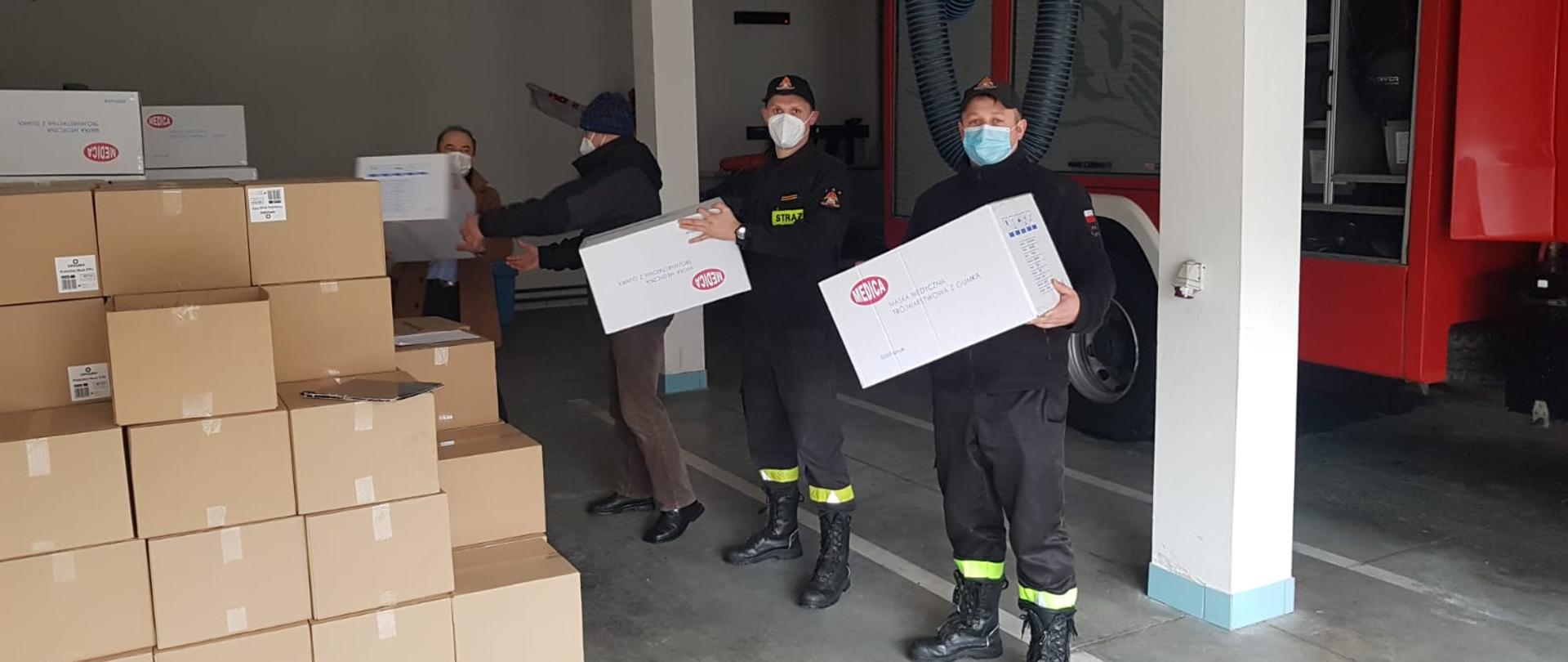 Na zdjęciu widoczni strażacy, którzy pomagają w rozdysponowaniu maseczek