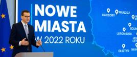 Premier przemawia na tle napisu: Nowe miasta w 2022 roku.