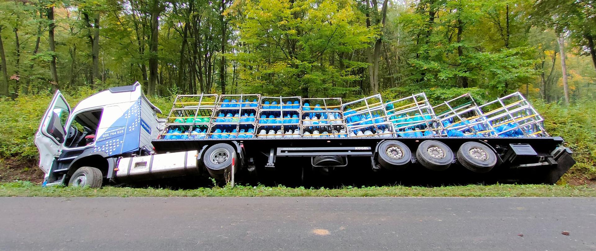 Na zdjęciu widać samochód ciężarowy przewożący butle propan-butan.W tle las.