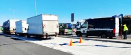 Pojazdy skontrolowane przez inspektorów z legnickiego oddziału ITD. Po lewej dwa busy i pojazd ciężarowy. Po prawej inspekcyjny furgon i inspektor ITD. W tle zaparkowane na przydrożnym parkingu samochody ciężarowe.