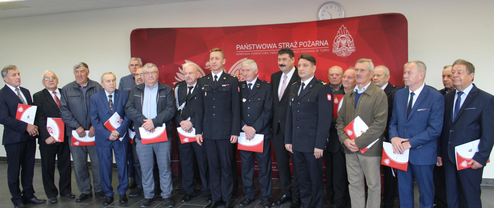 zdjęcie grupowe strażaków i mężczyzn na tle czerwonego baneru