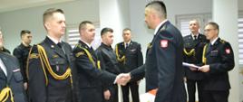 Komendant Powiatowy PSP wręcza akty mianowania strażakom ustawionym w szeregu. w tle strażacy