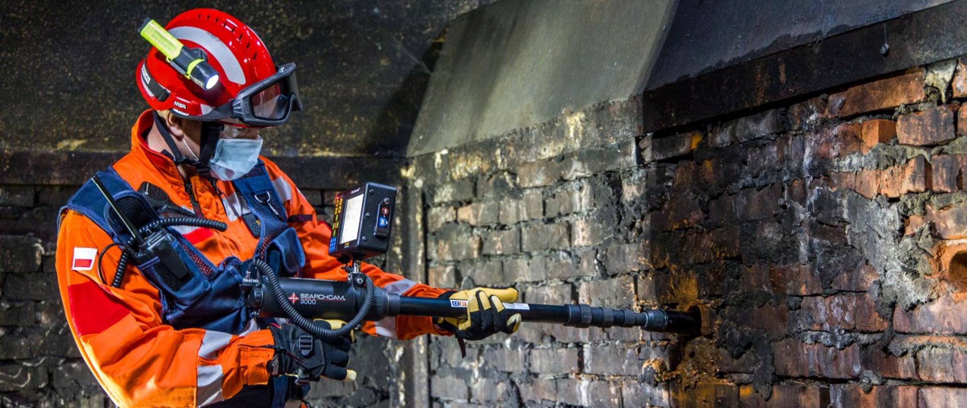 Strażak PSP sprawdzający przestrzeń za ścianą przy pomocy kamery wziernikowej.