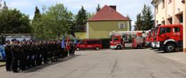 Pododdział stoi w dwuszeregu, za nim poczty towarzyszące. W tle samochody pożarnicze.