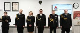 Strażacy stoją obok siebie podczas uroczystości jeden z nich czyta.