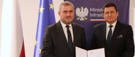 Wiceminister infrastruktury i nowy Szef ITD pozują do zdjęcia i przedstawiają akt nominacji. W tle ścianka z napisem Ministerstwo Infrastruktury.