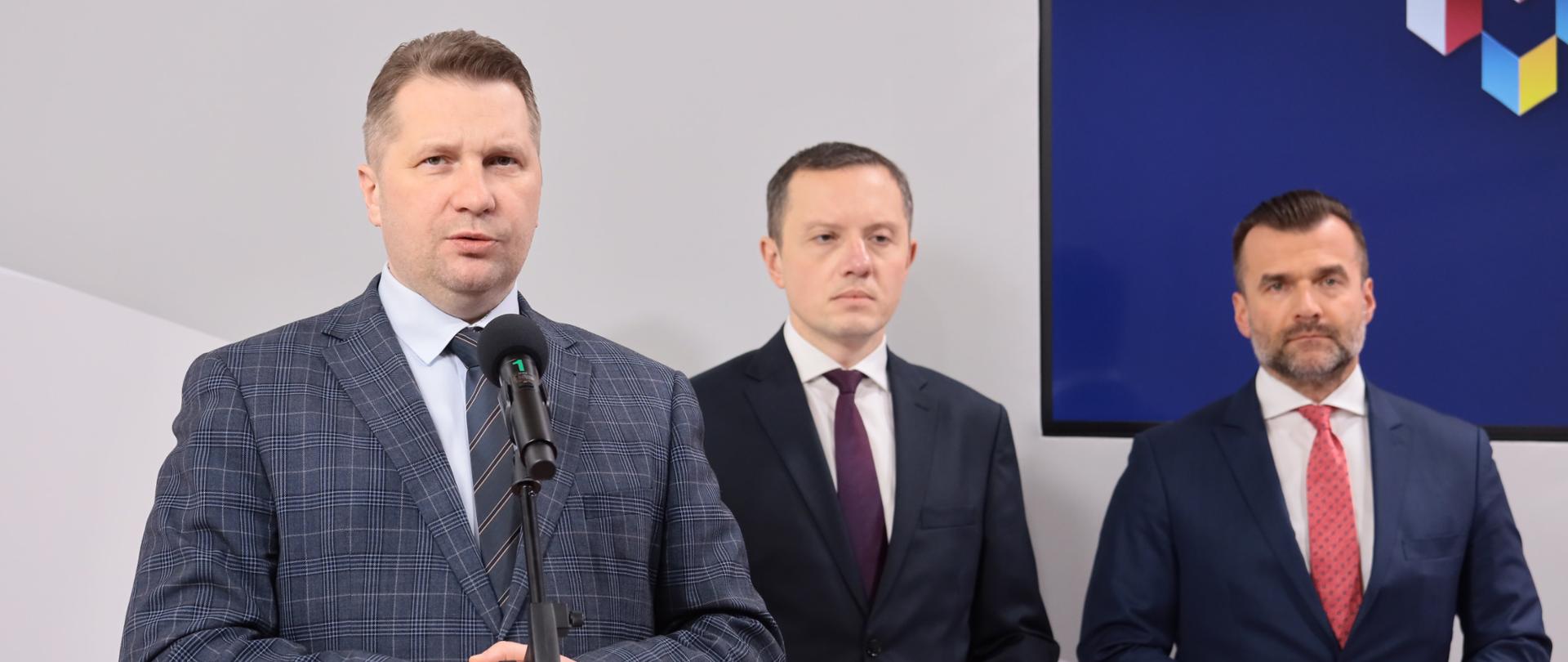 Minister Przemysław Czarnek przemawia podczas konferencji, stoi przed mikrofonem, za nim stoją prezes Poczty Polskiej Tomasz Zdzikot oraz prezes Związku Cyfrowa Polska Michał Kanownik.