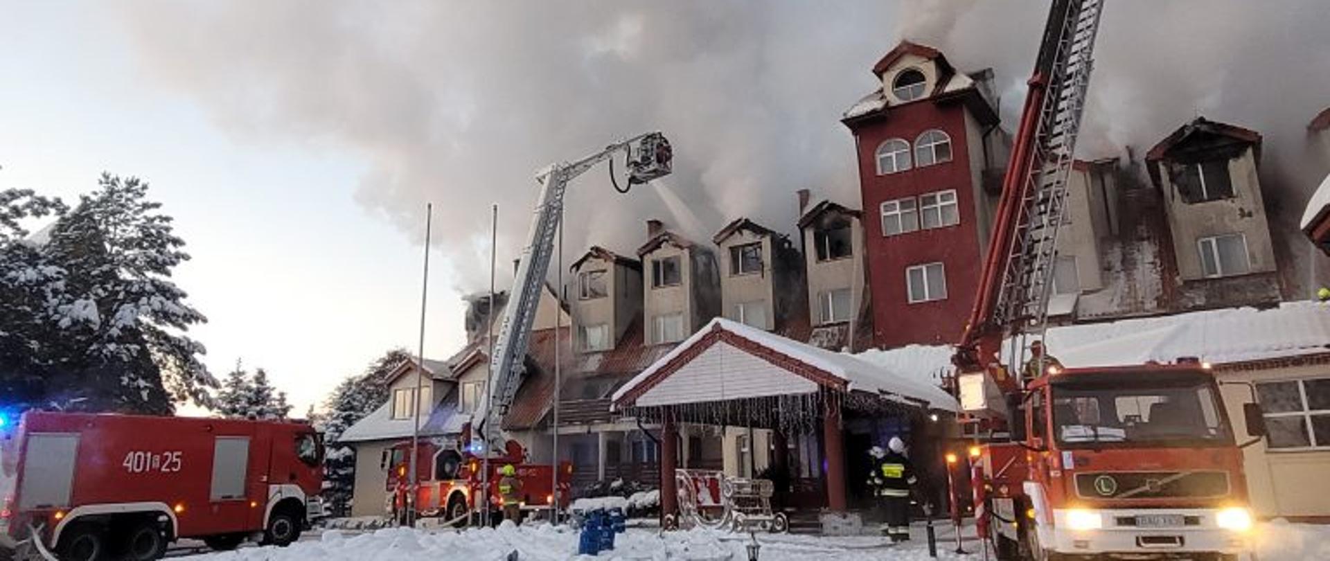 Zdjęcie przedstawiające strażaków i wozy pożarnicze podczas akcji gaśniczej płonącego budynku hotelu w miejscowości Augustów. 