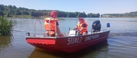Na zdjęciu widoczna jest łódź ratownicza straży pożarnej z oznaczeniem 511[E]Ł2, pływająca po zbiorniku wodnym. Na pokładzie znajdują się dwaj strażacy w kamizelkach ratunkowych i kaskach, wykonujący działania szkoleniowe. Tło stanowi spokojna tafla wody otoczona zielenią, co świadczy o działaniach prowadzonych w ramach ćwiczeń wodno-ratowniczych.