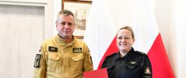 Pomorski komendant wojewódzki Państwowej Straży Pożarnej wspólnie ze strażakiem stoją na tle flag. Pracownik trzyma czerwoną teczkę w ręce. 