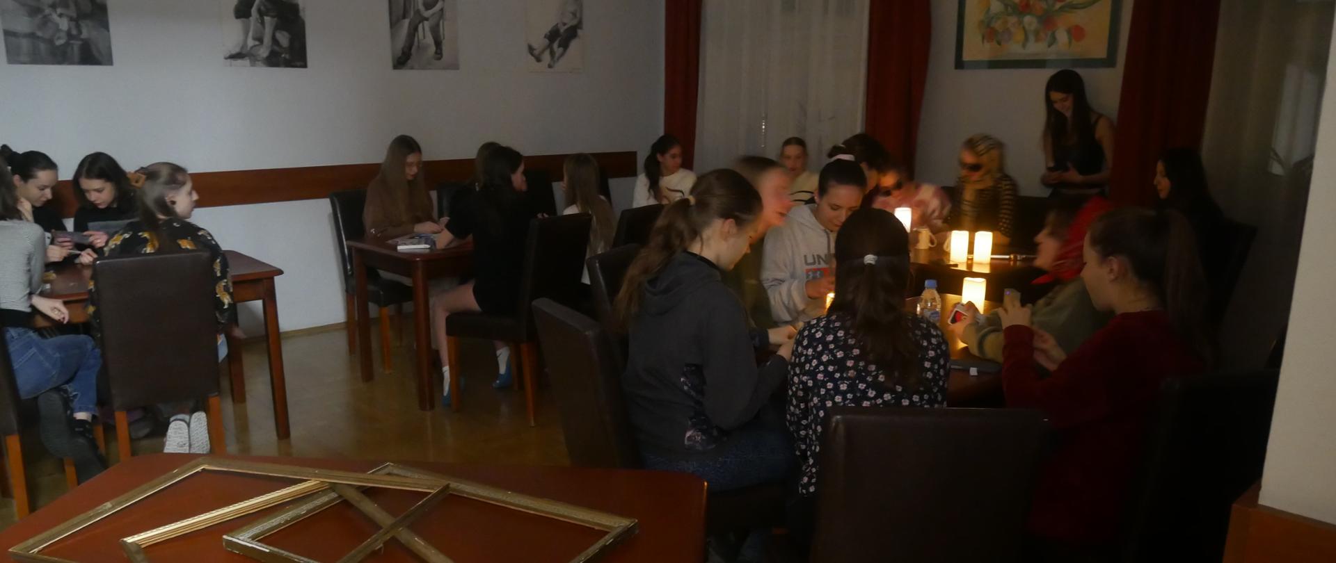 Wychowankowie zebrali się w świetlicy. Siedzą przy stolikach, na których stoją zapalone świece. Czekają na rozpoczęcie wróżb.