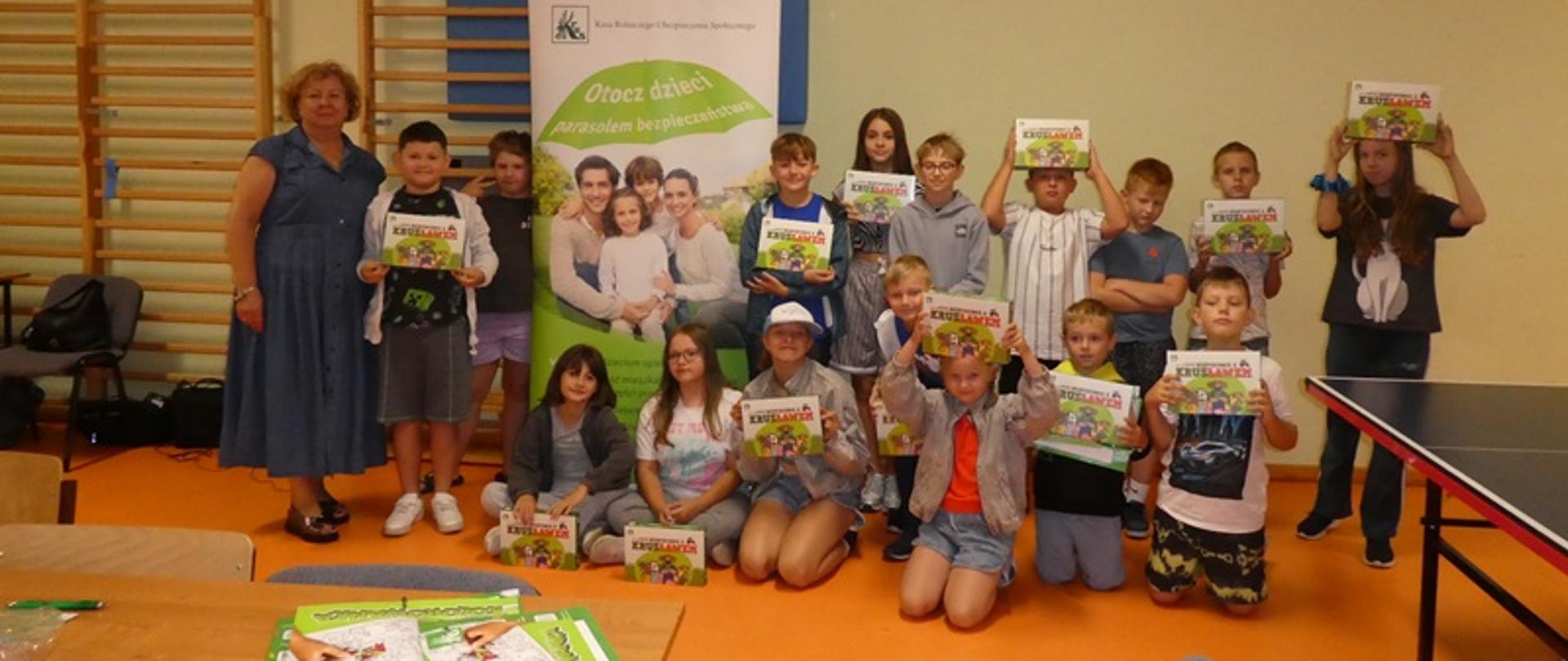 Na tle ściany i drabinek grupka dzieci stoi i trzymają w ręce czytanki