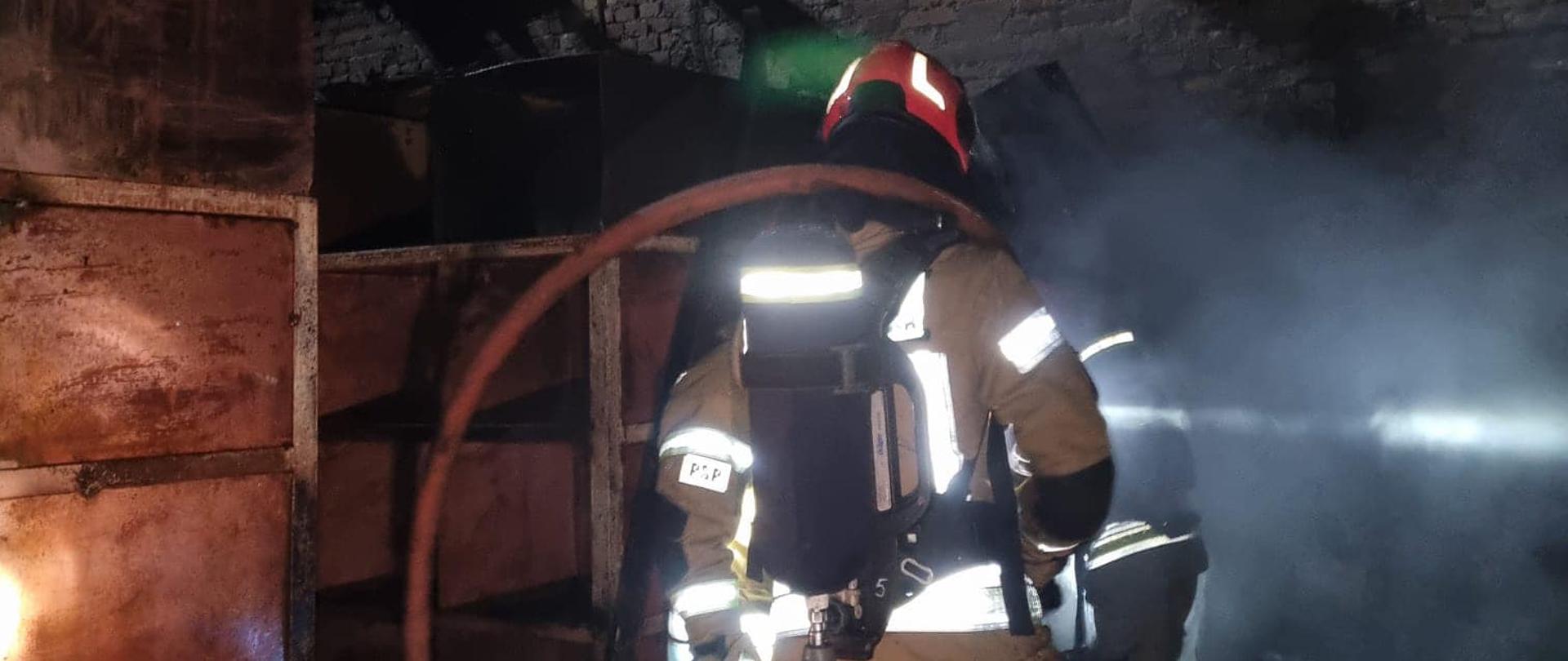 strażak z wężem strażackim na zgliszczach pożaru