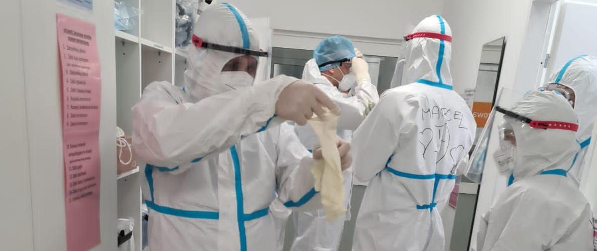 Strażacy PSP ratownicy medyczni ubrani w białe kombinezony w szpitalu w walce z COVID-19