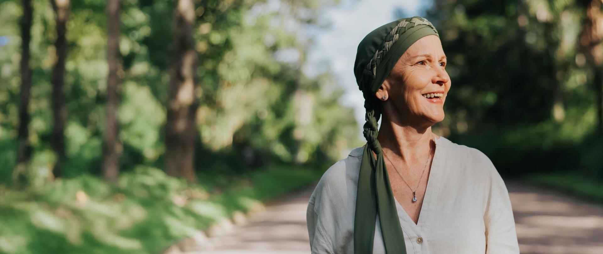 uśmiechająca się kobieta w średnim wieku z zieloną chustą na głowie, w tle las