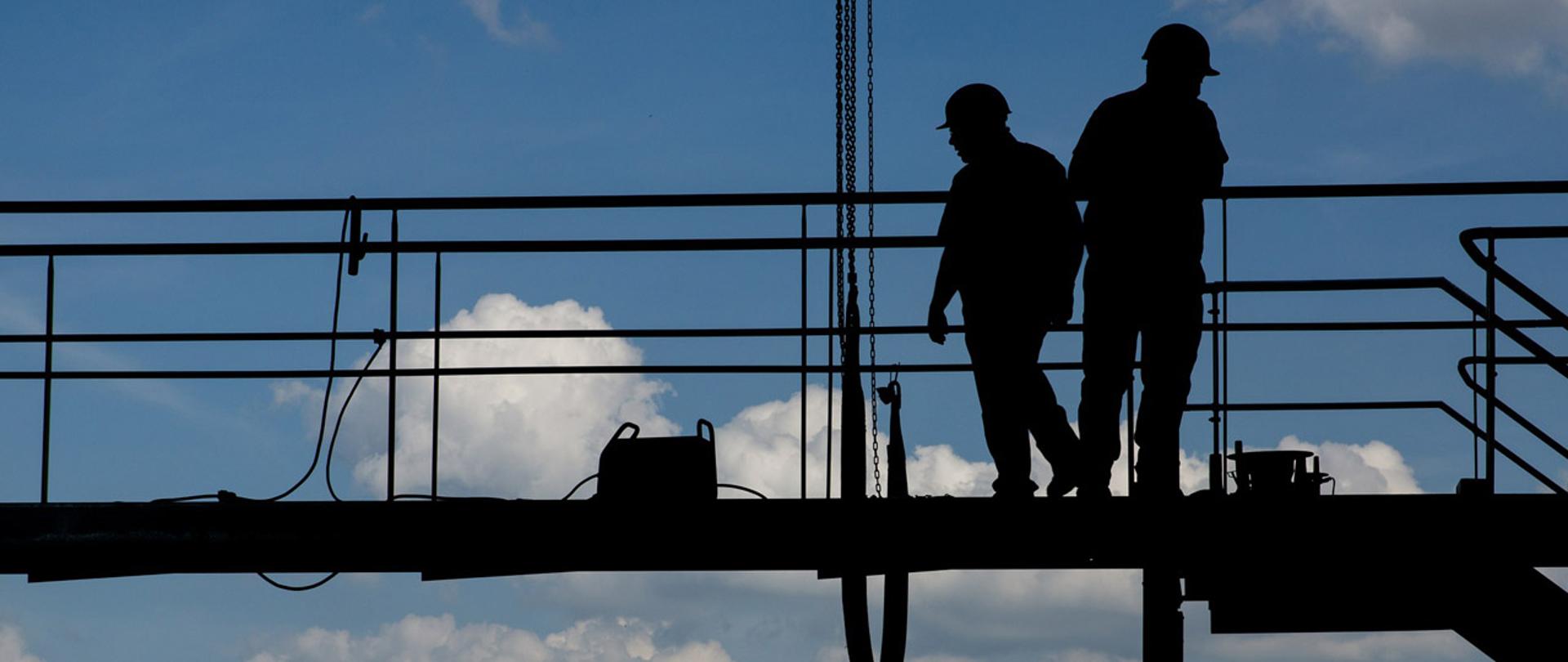 Sylwetki dwóch robotników na rusztowaniu