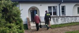 Strażak prowadzi starszą kobietę do punktu szczepień