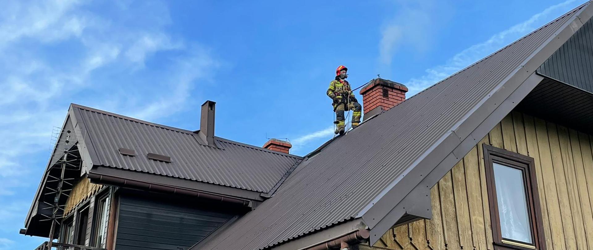 Strażak obok komina na dachu prowadzi działania