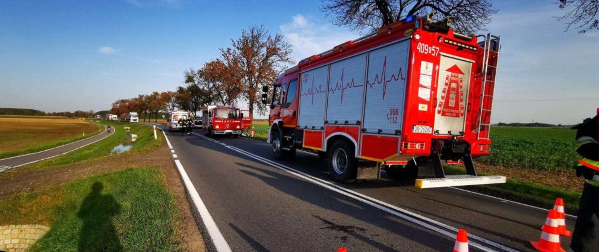 Zdjęcie przedstawia zamknięta drogę krajową nr. 39 na której znajdują się 2 pojazdy pożarnicze z OSP Lubsza oraz OSP Michałowice. W tle widoczny jest pojazd ZRM oraz samochód biorący udział w zdarzeniu.