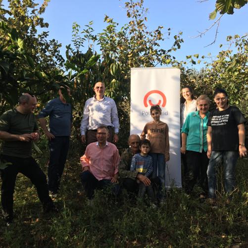 W sadzie na tle drzew stoi grupa dorosłych i dzieci i pozuje do zdjęcia obok baneru Polskiej pomocy