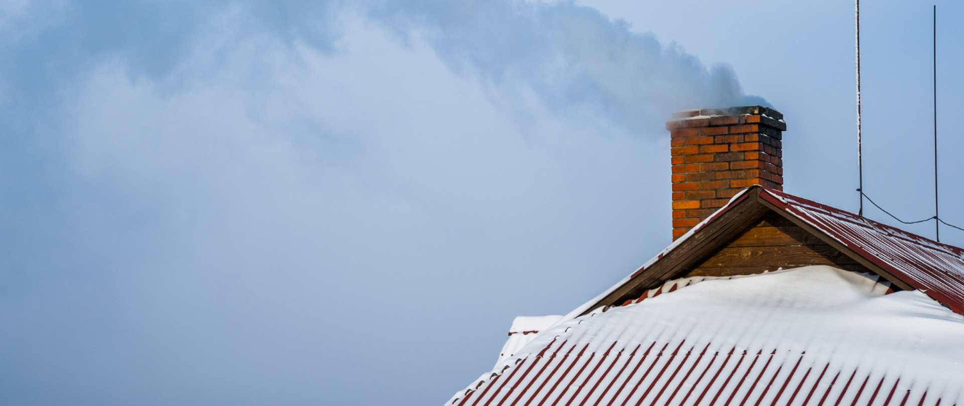 Zdjęcie dachu domu pokrytego śniegiem z kominem, z którego unosi się dym.