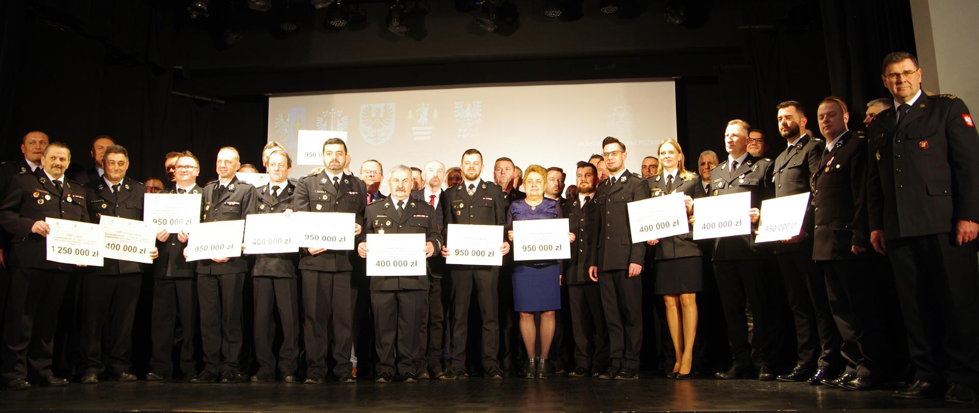 Widok ogólny z przodu – zdjęcie zbiorowe. Wszyscy uczestnicy uroczystości stoją na scenie GOK. 