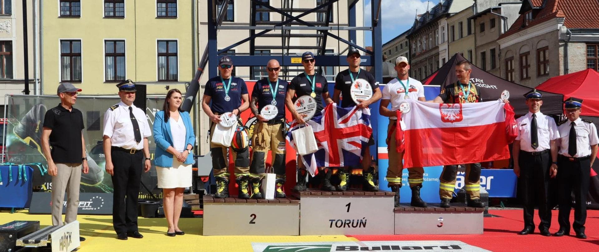 na podium stoją zawodnicy, obok osoby wręczające nagrody.