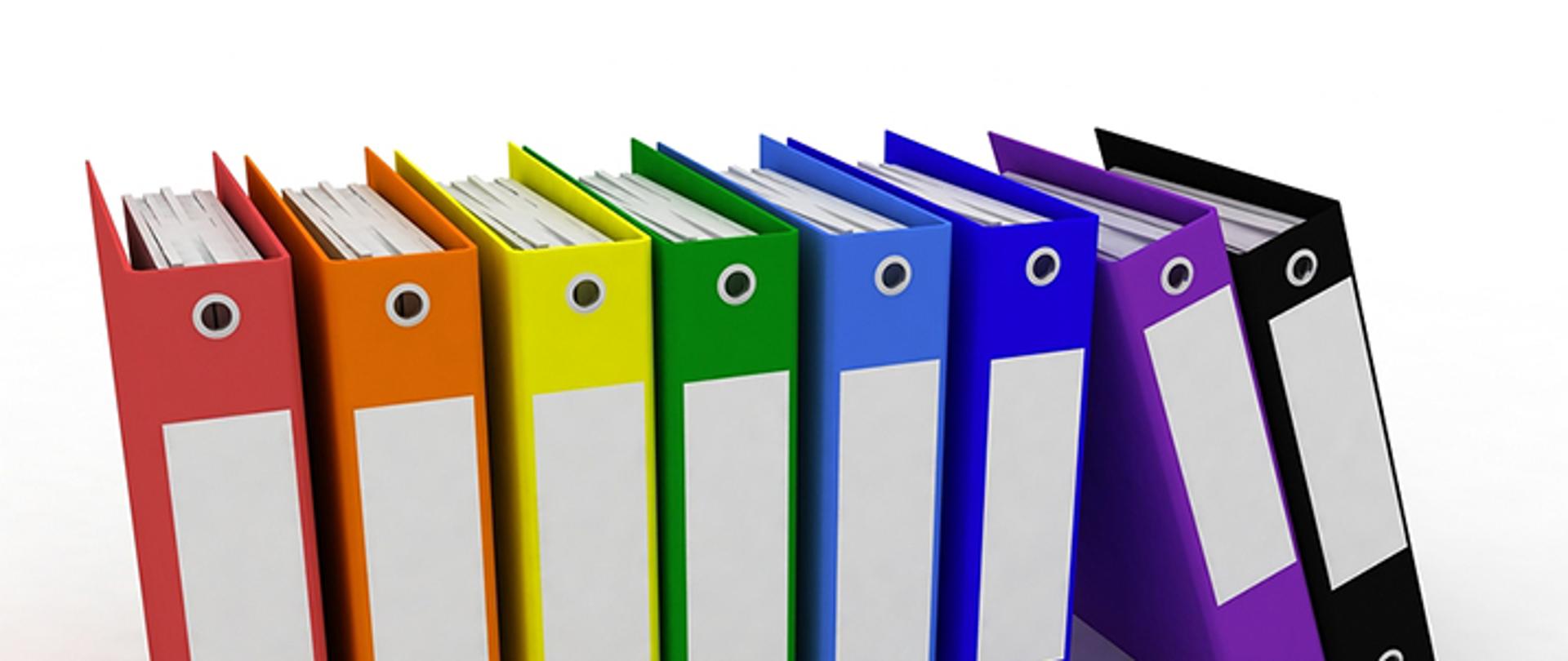 Fotografia przedstawiająca sześć stojących kolorowych segregatorów z dokumentami oraz dwoma opierającymi się o nie segregatory. Całość na białym tle z efektem lustrzanym na dole.