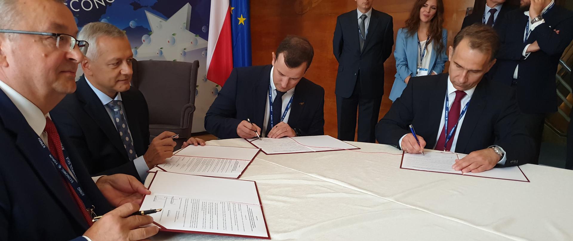 Ministrowie Marek Zagórski i Andrzej Adamczyk podpisują dokumenty siedząc przy stole.
