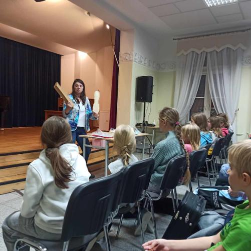 Fotogaleria z warsztatów lutniczych. Na zdjęciu lutnik pokazuje jak powstają skrzypce, jakie materiały służą do konserwacji instrumentu. Na sali jest dużo obserwatorów - uczniów szkoły muzycznej.