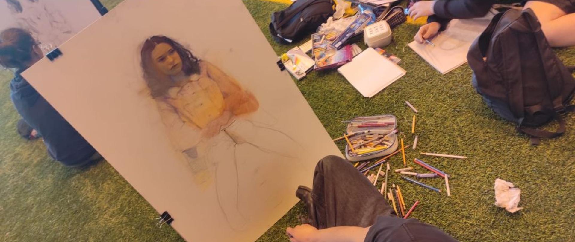 Rysunek młodej dziewczyny w trakcji tworzenia, obok rozrzucone kredki