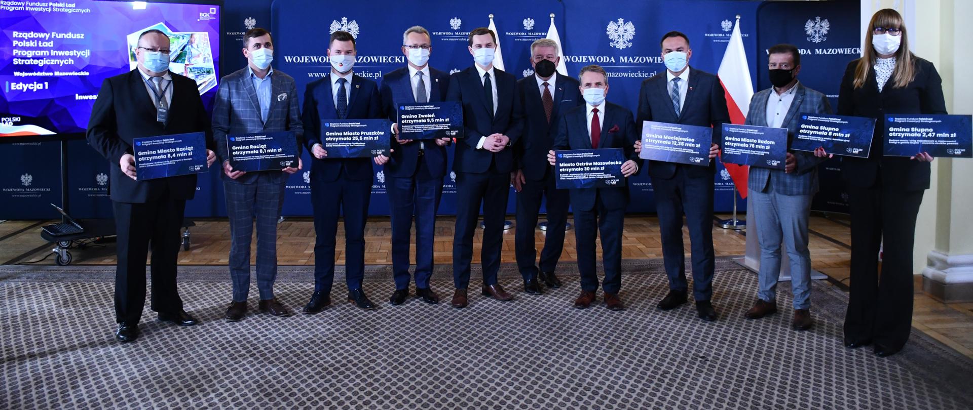 Na zdjęciu znajduje się dziesięć osób, osiem z nich trzyma symboliczne czeki Polskiego Ładu