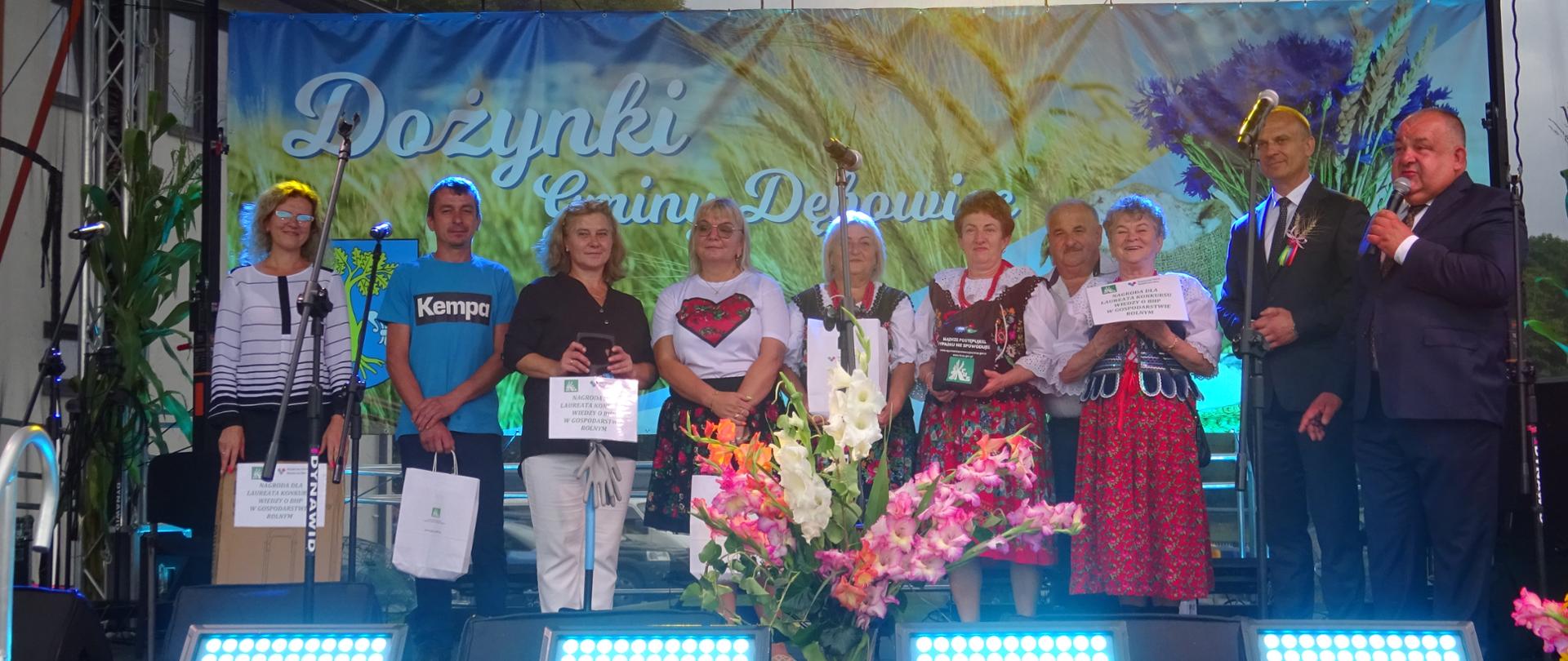 Na scenie stoi grupa osób, od lewej są to: laureaci i osoby wyróżnione w konkursie, którzy trzymają w rękach nagrody, po prawej dwaj przedstawiciele KRUS. Jeden z nich trzyma mikrofon.