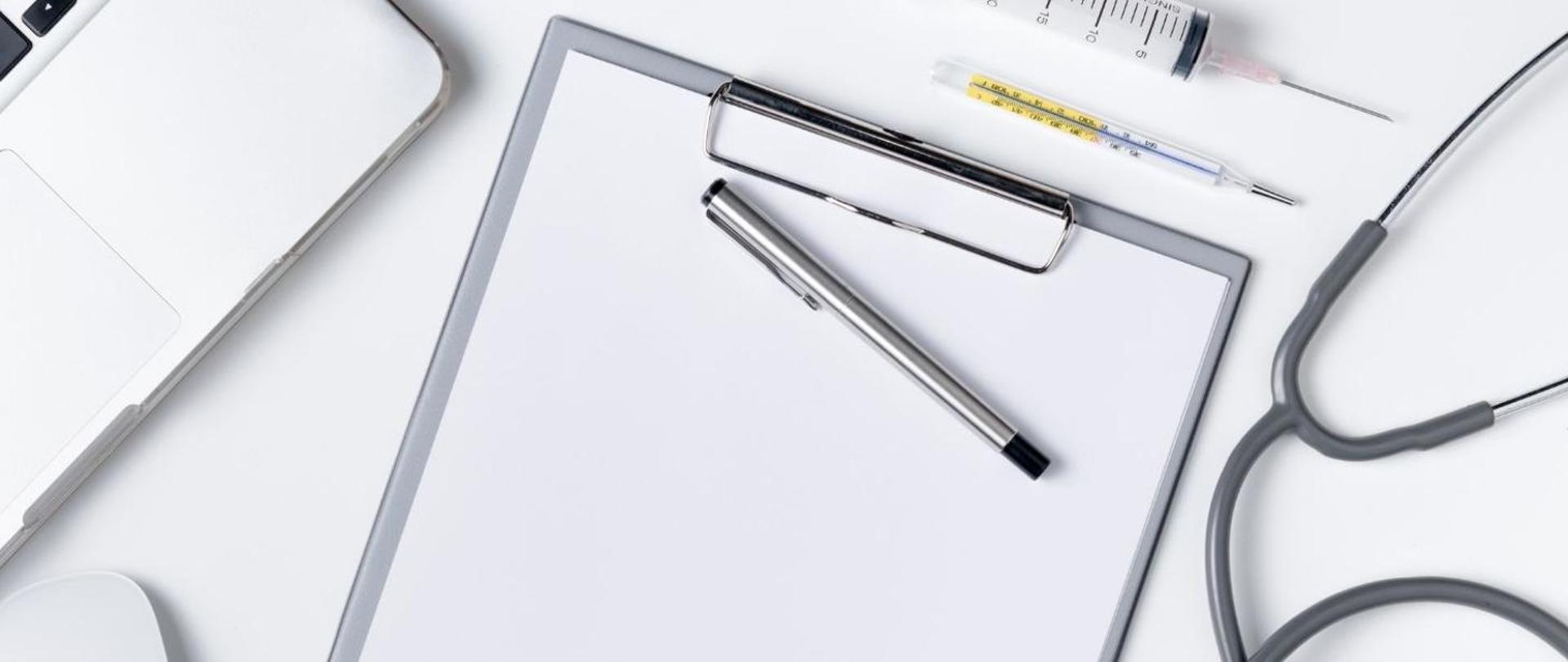 Na zdjęciu widać na białym biurku organizer, słuchawkę lekarską i pióro.